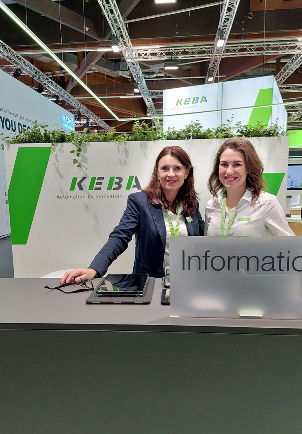 Two people standing at an information and reception counter at a trade fair booth, assisting visitors with information about automation solutions.