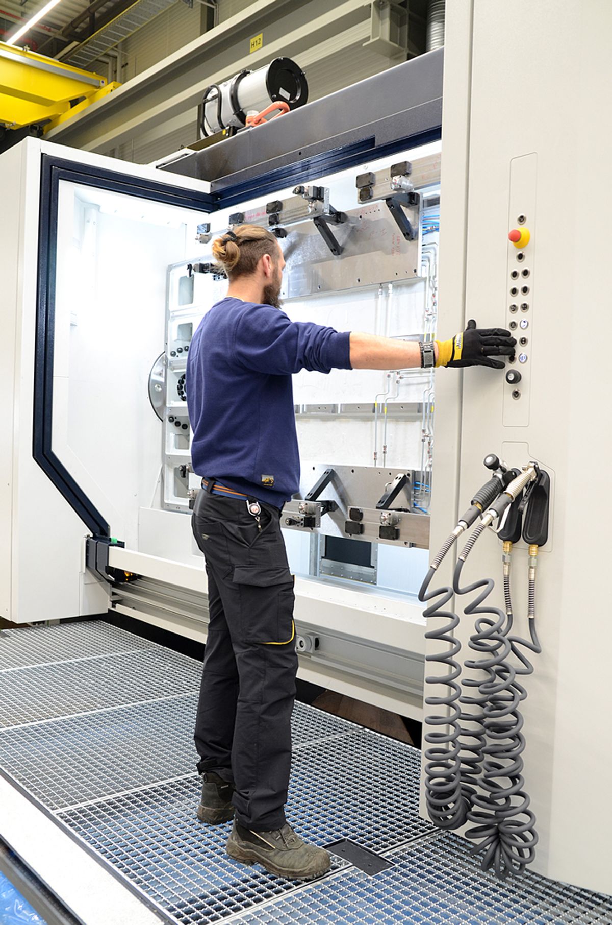 A machine operator standing at an industrial system operating a side control panel with buttons and an emergency stop switch – example of precise machine control and safe production processes.
