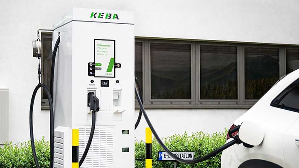 KEBA charging station charging a white electric car in front of a modern building.