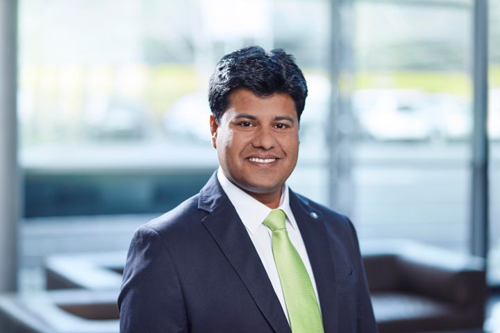 Portrait of a smiling manager in a dark business suit with a light green tie, standing in a modern office environment. The image conveys leadership and executive responsibility in industrial automation.