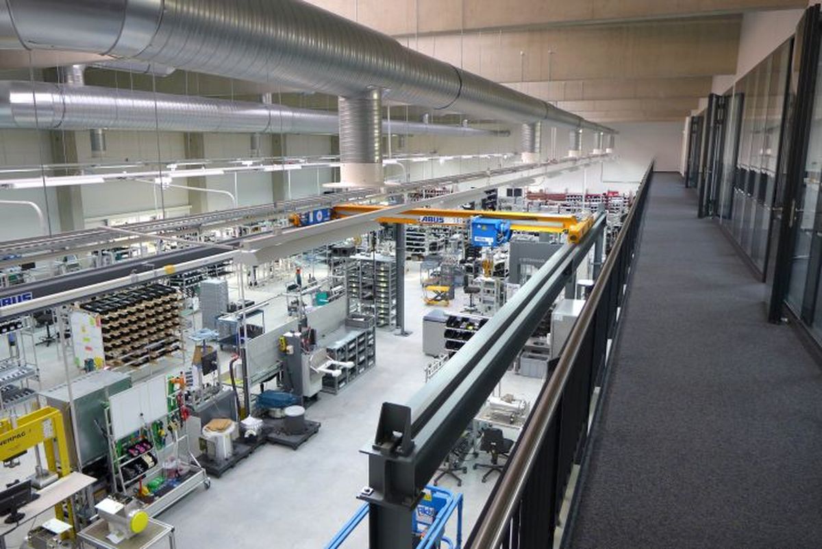 Blick von der Galerie auf die modern ausgestattete Produktionshalle von KEBA mit zahlreichen Arbeitsplätzen, Maschinen und einem Deckenkransystem.