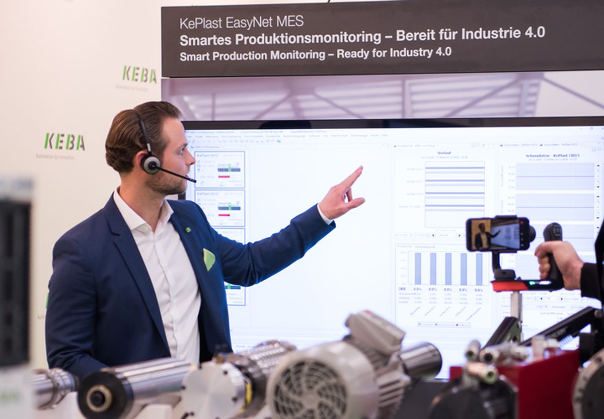 KEBA employee stands behind an exhibit at a booth..