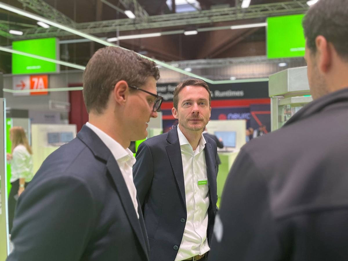 Several people engaged in a professional discussion at a trade fair booth about industrial automation solutions.