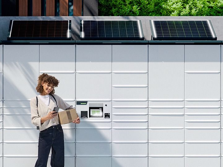 荷物を手にした女性がKEBAのPaketstationの前に立っている。