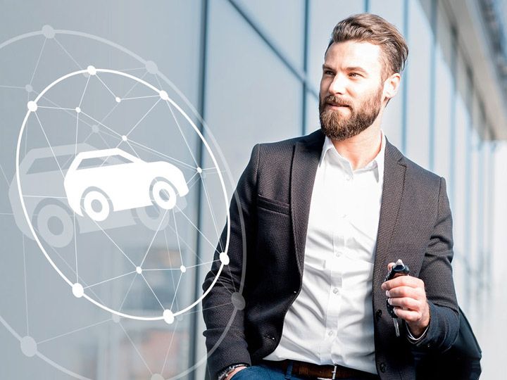 Businessman with car key in front of a building, with a connected mobility icon on the left.