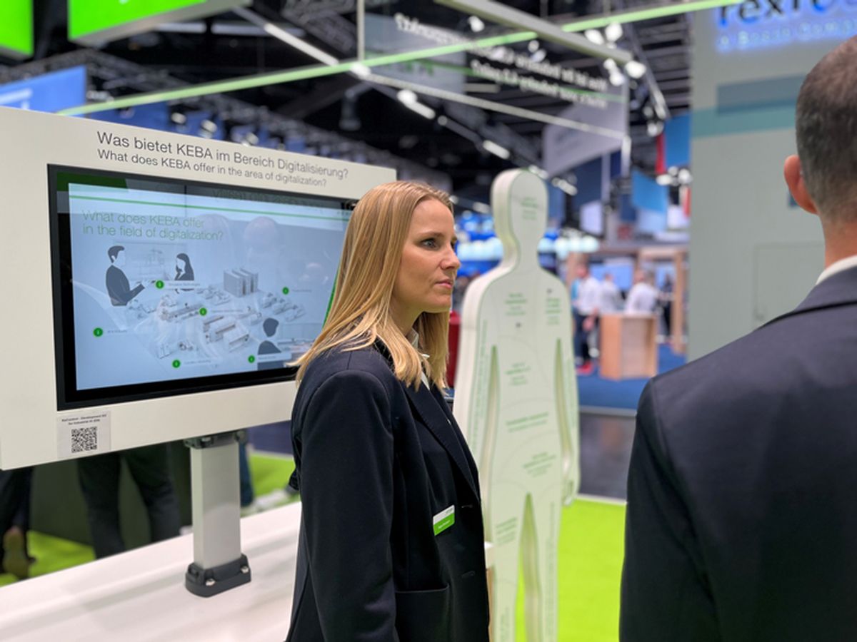 A person standing in front of an information display explaining topics related to digitalization and automation to visitors.