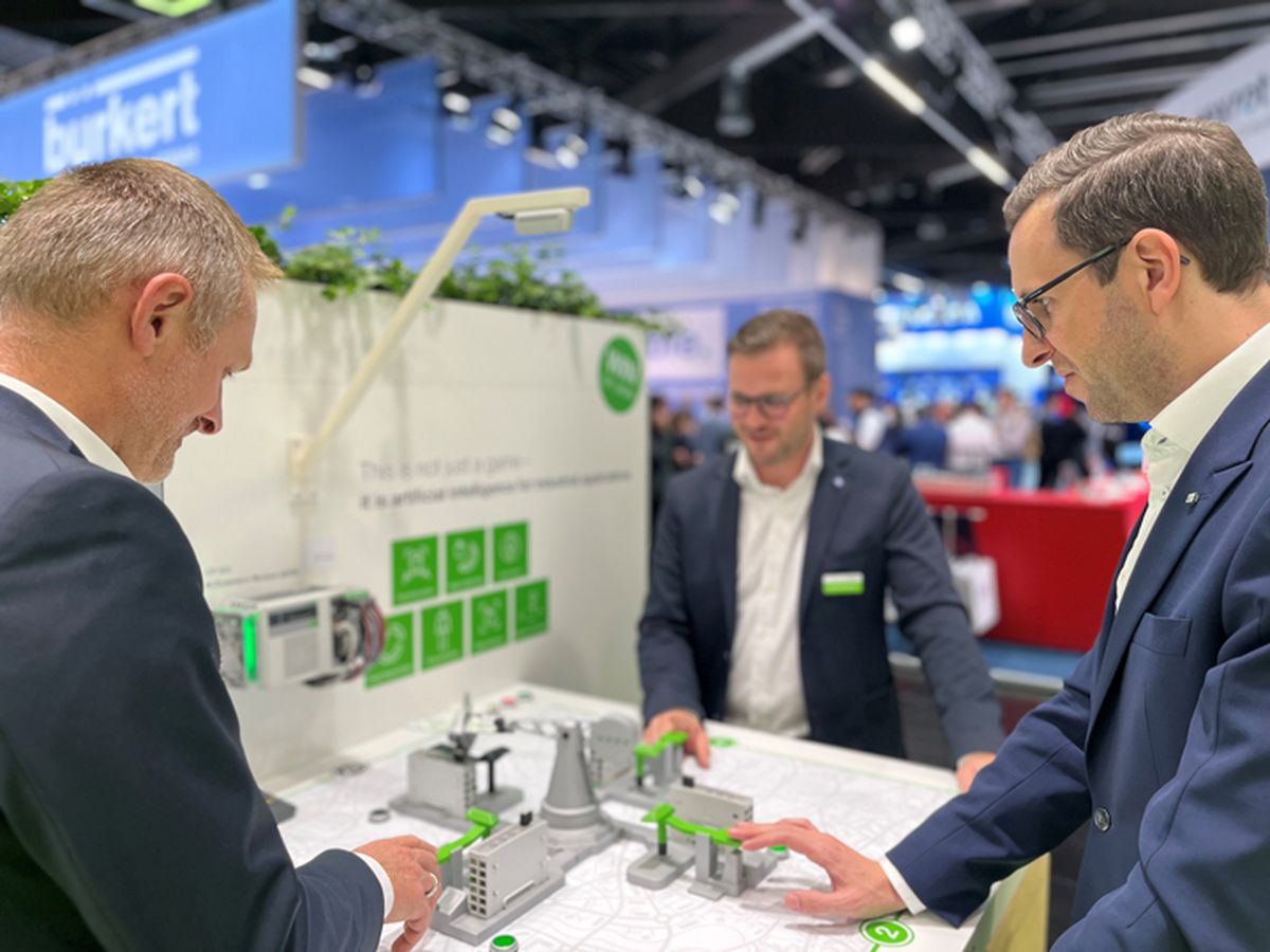 Three people standing at a demonstration model discussing automation concepts and system interactions.