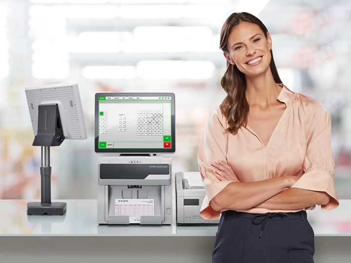 Lächelnde Frau in pfirsichfarbener Bluse steht neben dem Lotto-Terminal KeWin multimedia auf einem Tresen.