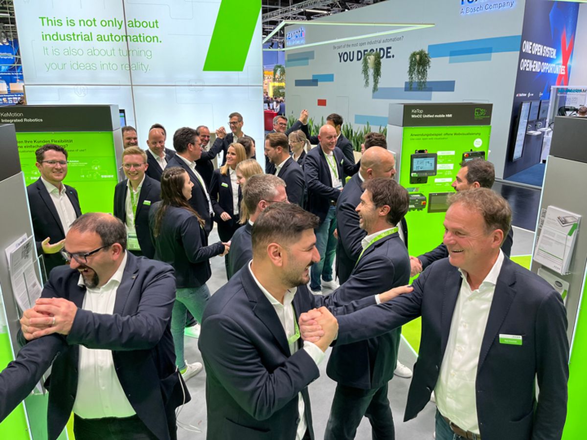 Larger group of people interacting at a trade fair booth, illustrating teamwork, networking, and presentation of automation solutions.