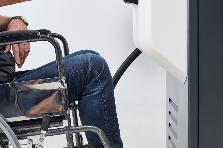 Eine Person im Rollstuhl bedient die KeContact DCA20. Die Aufnahme zeigt die barrierefreie Erreichbarkeit der Bedienelemente aus sitzender Position.