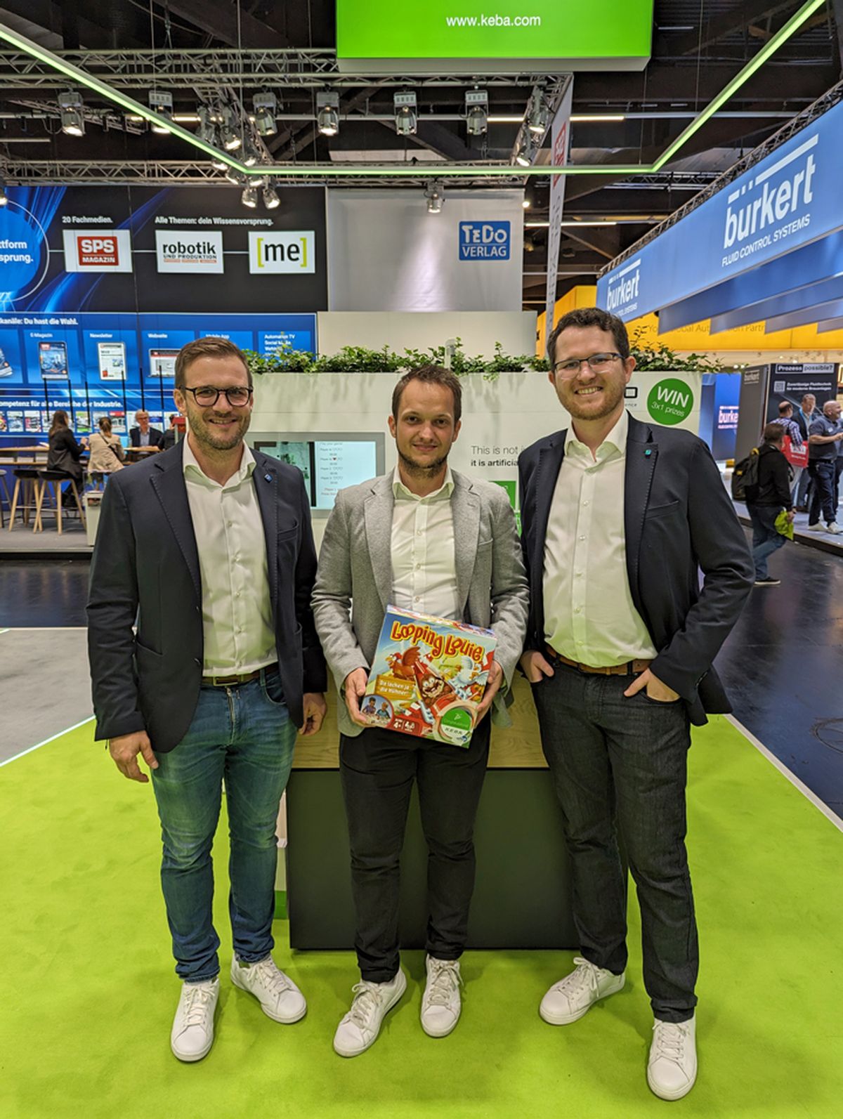 Three people standing together at a trade fair booth holding a prize or promotional item as part of an exhibition activity.