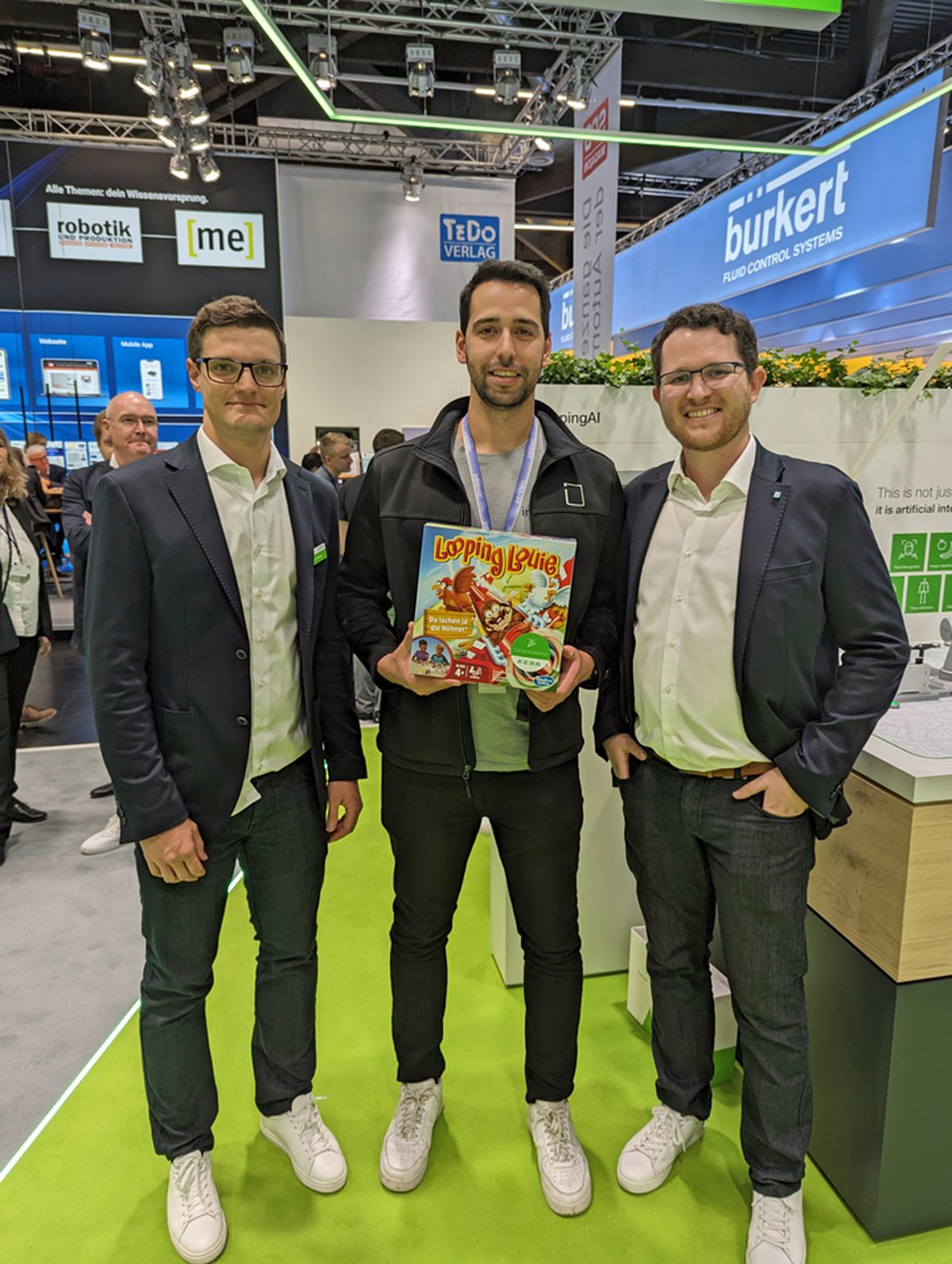 Three people standing together at a trade fair booth holding a prize or promotional item as part of an exhibition activity.