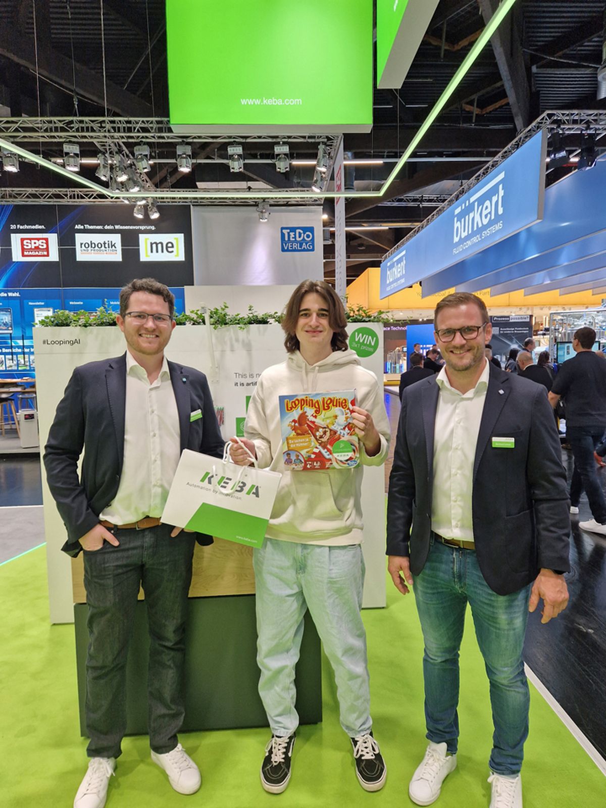 Three people standing together at a trade fair booth holding a prize or promotional item as part of an exhibition activity.