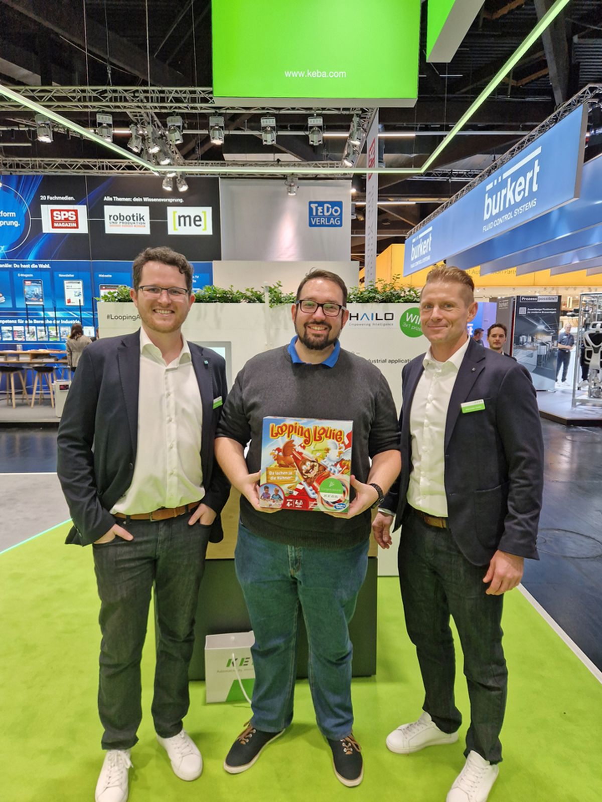 Three people standing together at a trade fair booth holding a prize or promotional item as part of an exhibition activity.