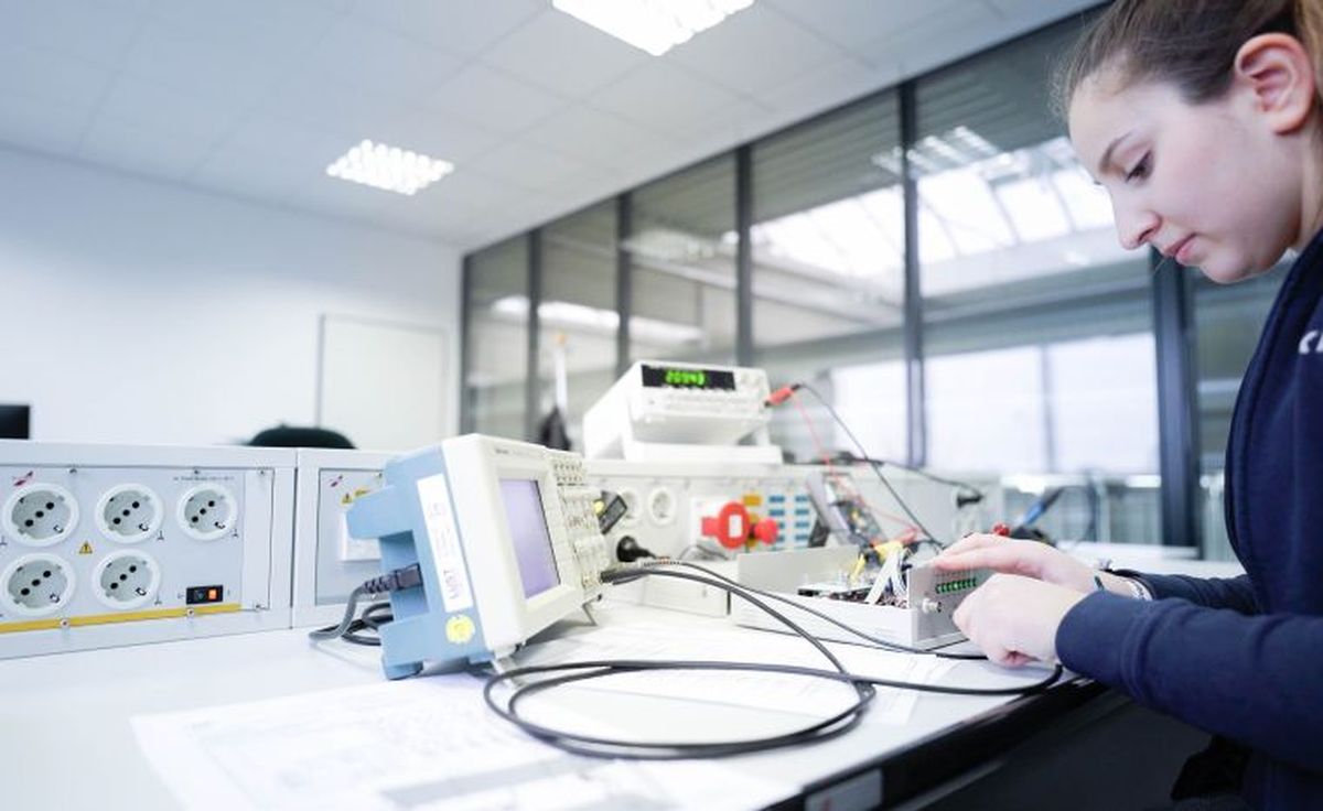 Eine KEBA-Auszubildende arbeitet konzentriert an einem Prüfstand mit Oszilloskop, Netzteil und Schaltungen in einem modern ausgestatteten Elektroniklabor.