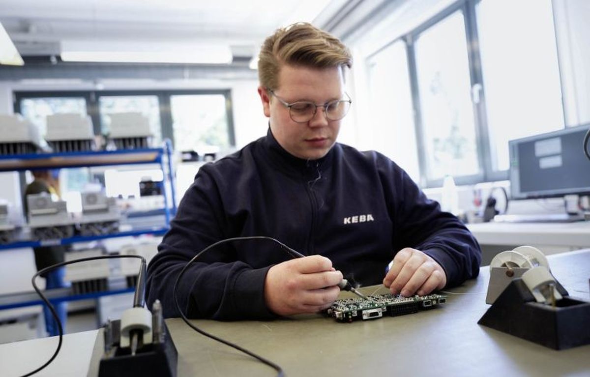 Ein KEBA-Auszubildender konzentriert sich im Elektroniklabor auf die präzise Prüfung einer Leiterplatte