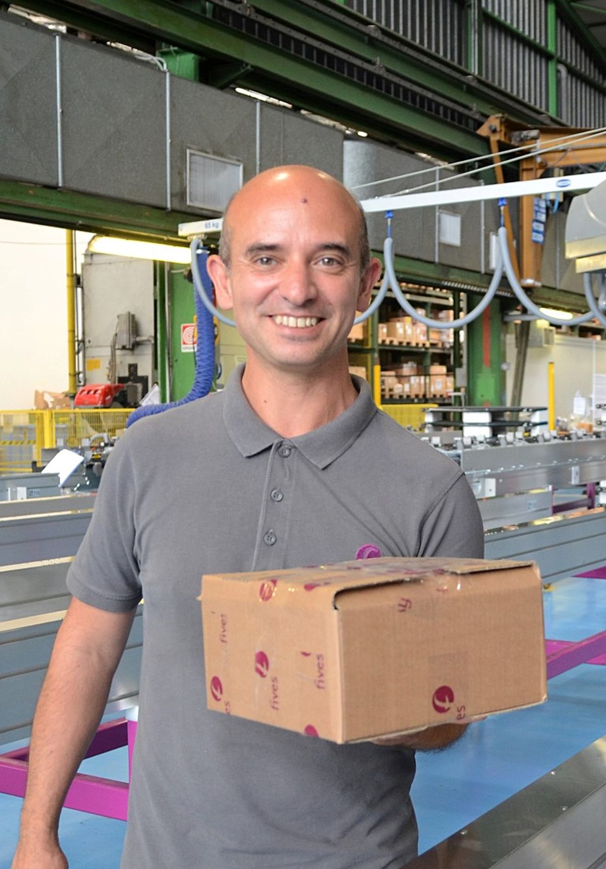 Dipendente in un impianto di produzione che tiene un pacco e sorride alla fotocamera – simbolo di lavoro di squadra, affidabilità e impegno nella produzione industriale.