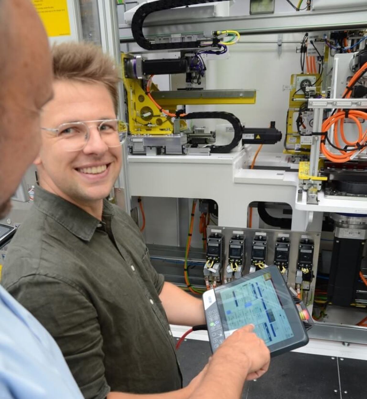 A technician operates an automated system using a mobile control panel while smiling at the camera. The image highlights modern machine control, intuitive HMI operation, and enthusiasm for technological innovation.