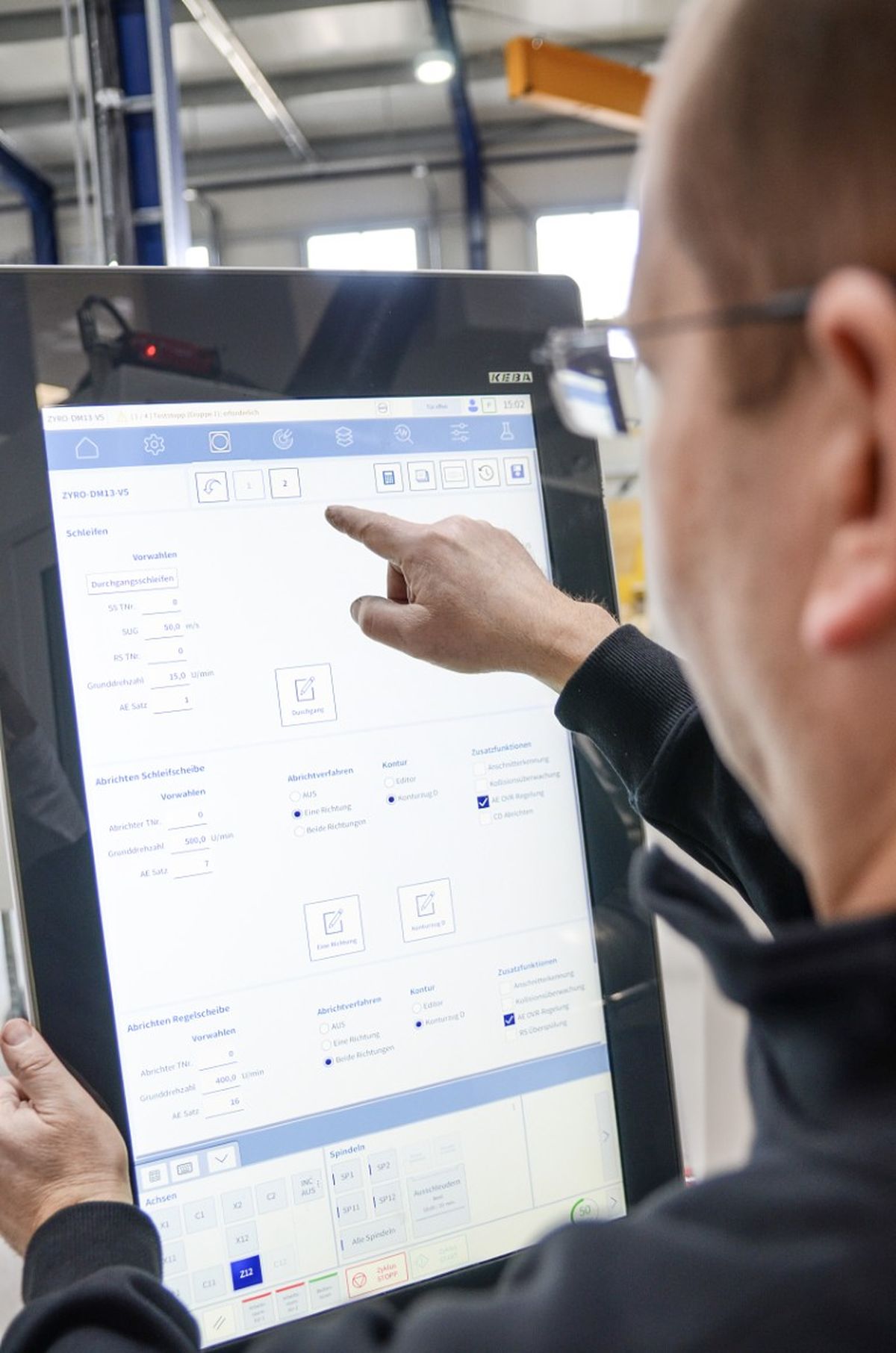 Close-up of a hand pointing at an HMI display to select a function. The screen shows detailed control and process information.