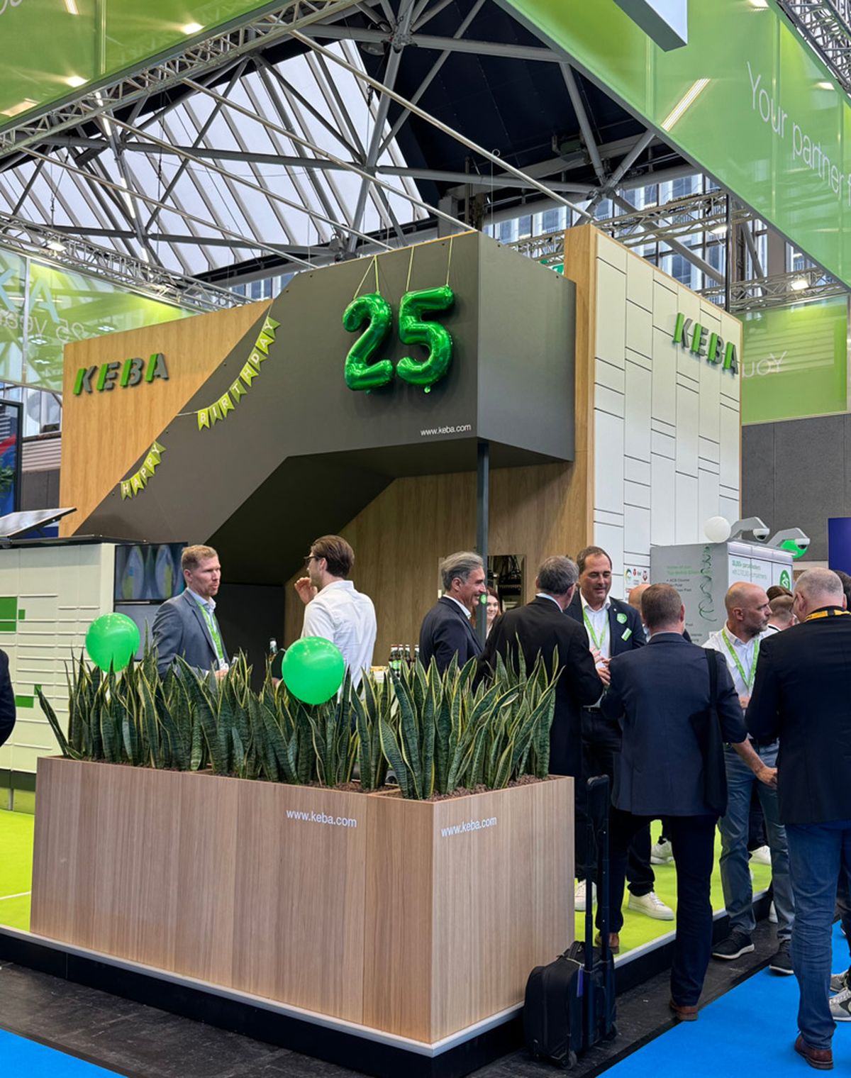 People gathered at a booth with green balloons and a large "25" decoration.