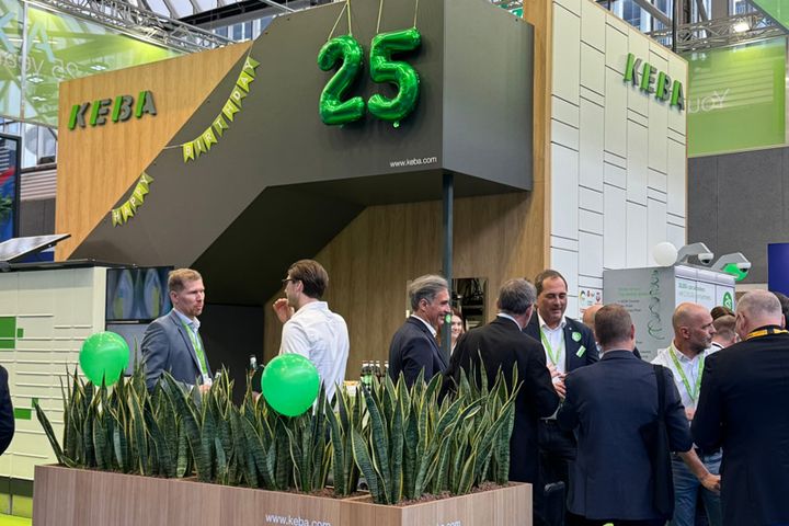 People gathered at a booth with green balloons and a large "25" decoration.
