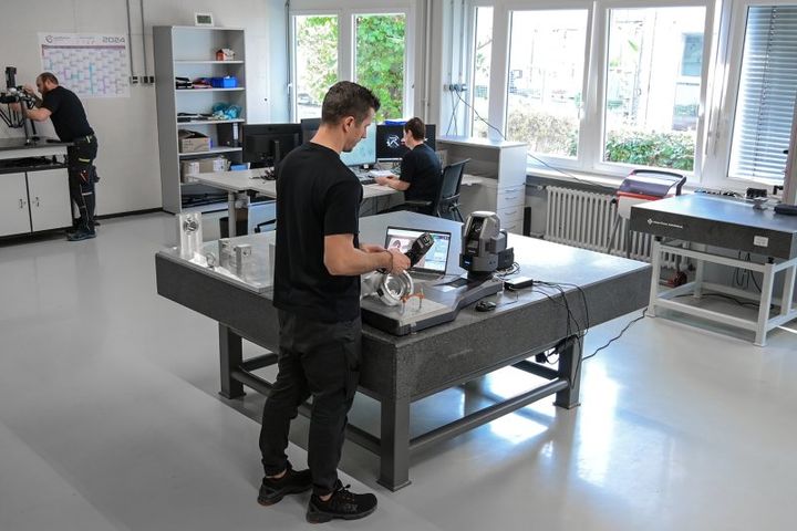 An autonox employee performs quality control on a robot mechanism. In front of him are a laptop and a 6-axis robot.