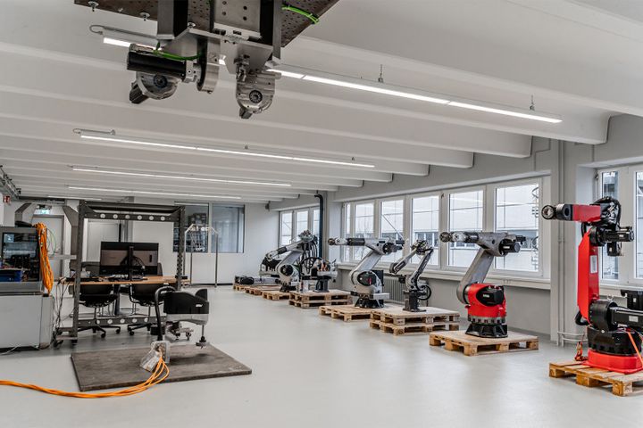 The development laboratory at autonox Robotics. Various 6-axis robot mechanisms can be seen on the right. On the left is a robot cell, a desk with a screen, and a Scara robot mechanism in the foreground, connected by an orange cable.