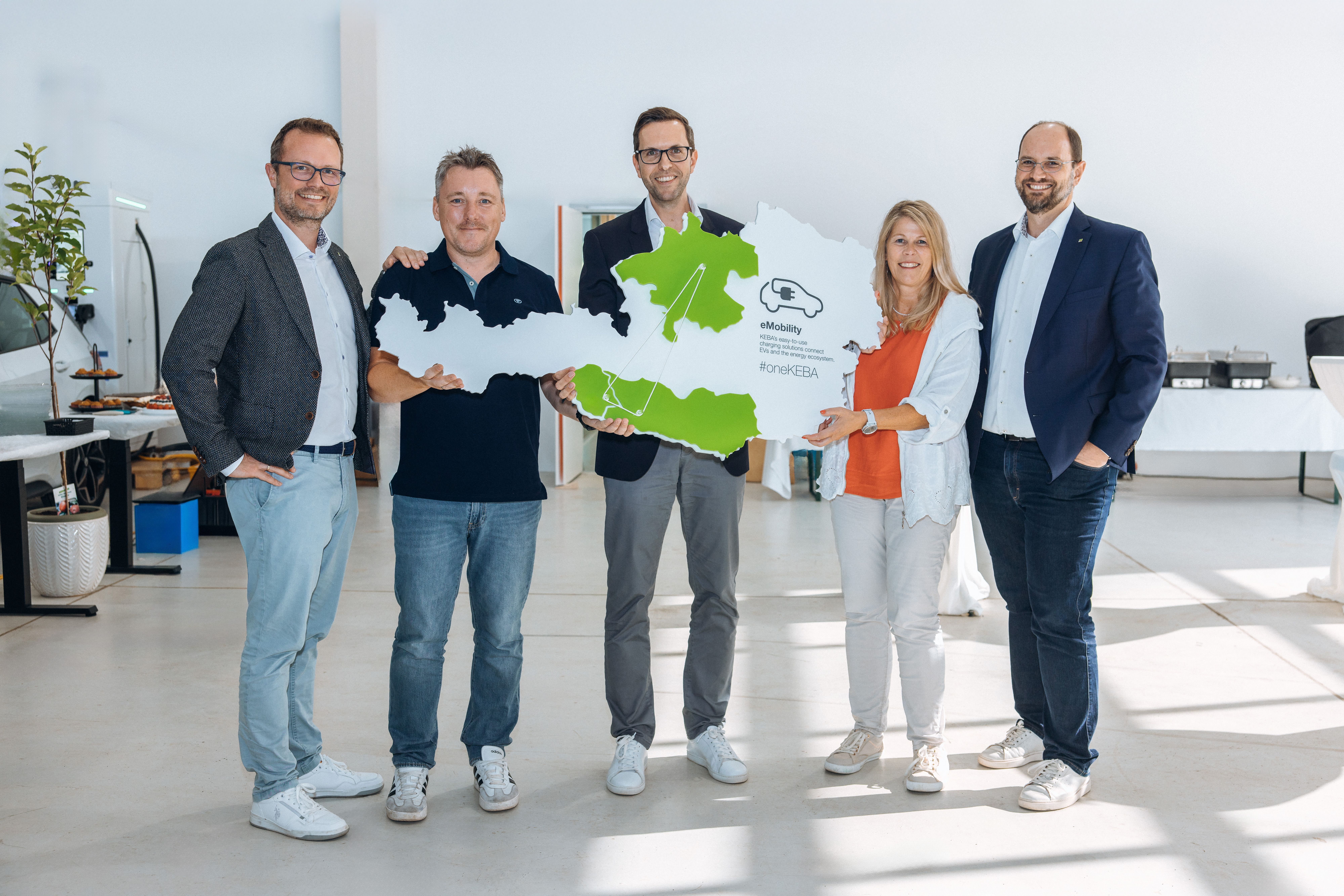 Five KEBA team members holding a large map of Austria with highlighted eMobility locations during the opening of the new development site in Kötschach-Mauthen.