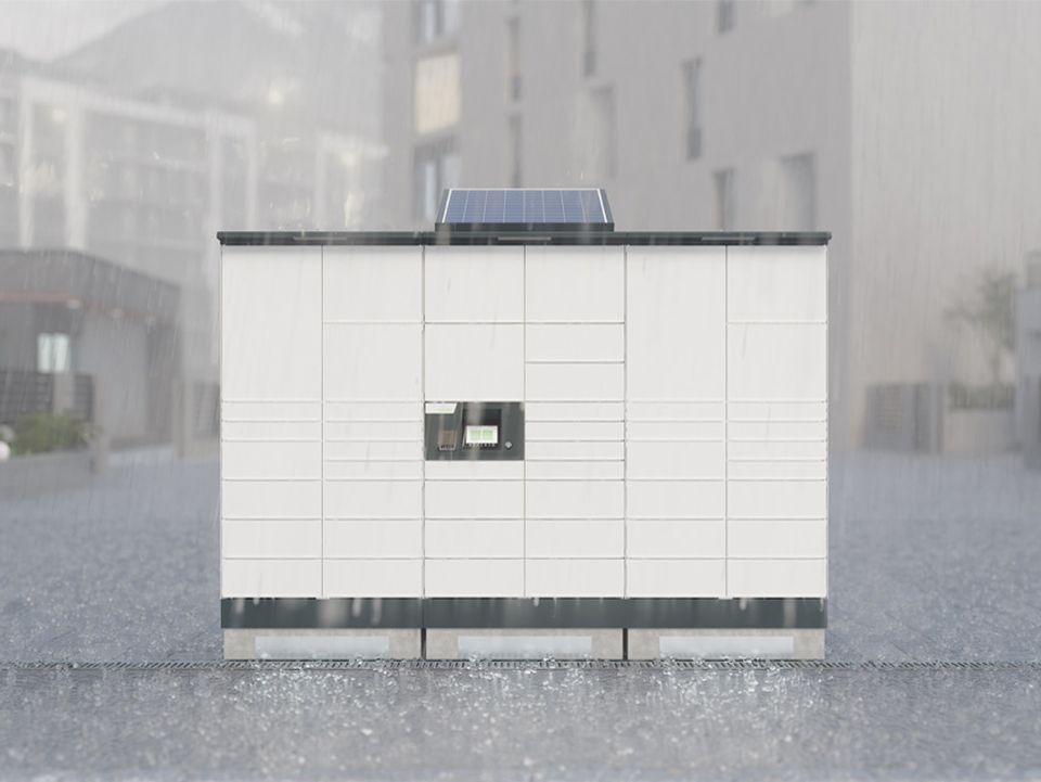 Moderne Paketstation mit Solarpanel auf dem Dach in regnerischer urbaner Umgebung, unscharfe Strukturen im Hintergrund.