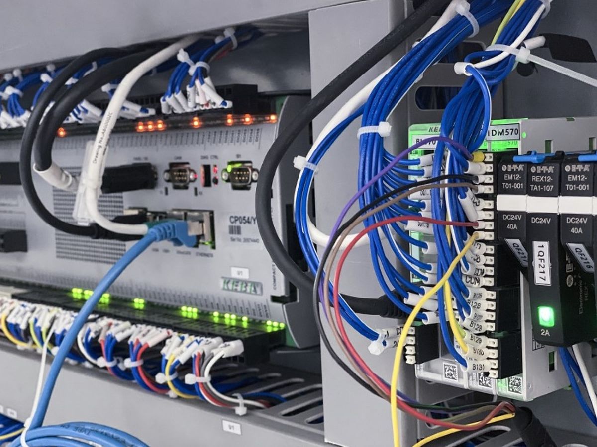 Detailed view of a machine control cabinet showing neatly organized blue, white, and yellow wires connected to terminals and labeled components, with indicator lights glowing.