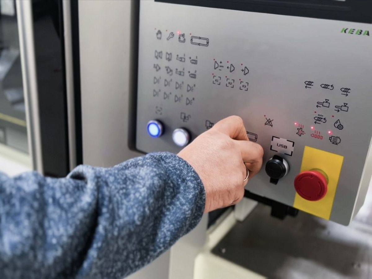 Person operating a control panel with various buttons and switches, wearing a blue sweater.