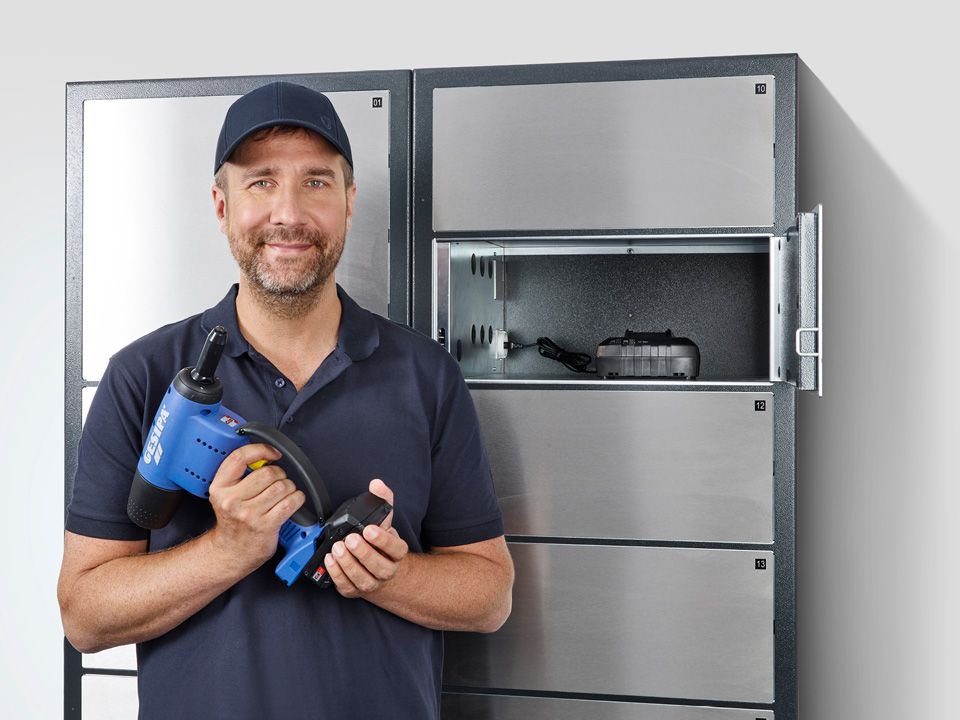 Elektronisches Schlüsselverwaltungsfach in dem ein Prüfwerkzeug liegt. Davor steht ein Mann mit einem Werkzeug in der Hand.
