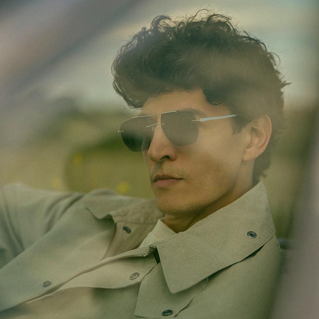 Nacho wearing Nova Shades, driving with a focused expression behind the wheel.