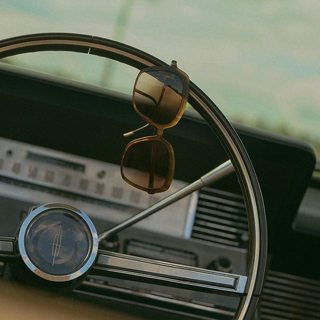 Close-up of Nova Shades hanging on the steering wheel of a vintage car.