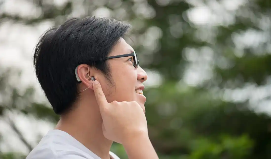 A man positions the speaker from his RIC hearing aid into his ear canal. The plastic filament pointing down is a retention filament that is placed into the "bowl" of the ear to stop the speaker from working its way out of the ear.