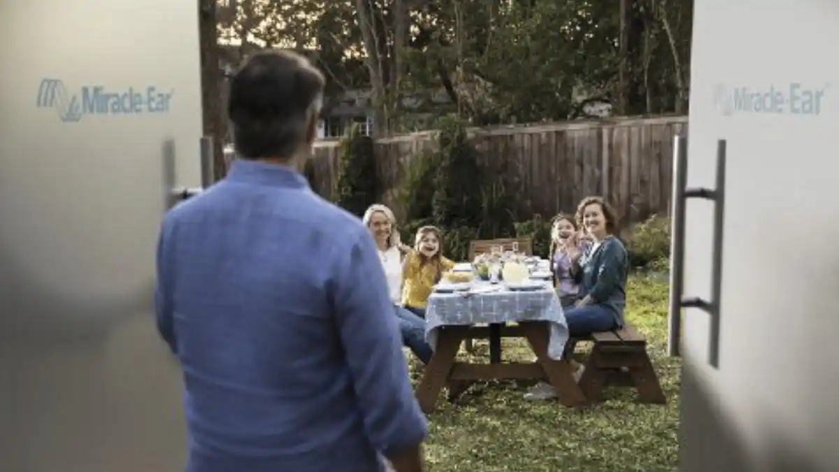 Photo of a man opening a door with Miracle-Ear logos onto a family picnic