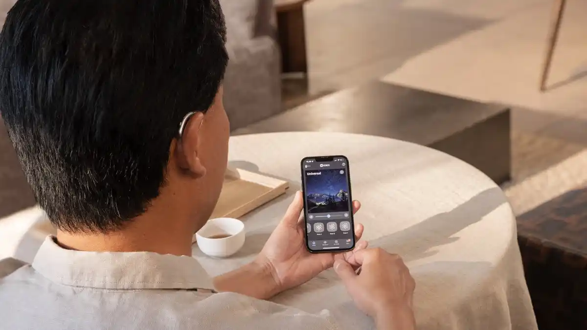 With most of the non-custom (over-the-ear) hearing aids offered at HearUSA, you can be fitted and walk out the door with the hearing aids on the same day. Here, a man adjusts his hearing aids in a cafe using the Widex MOMENT app.