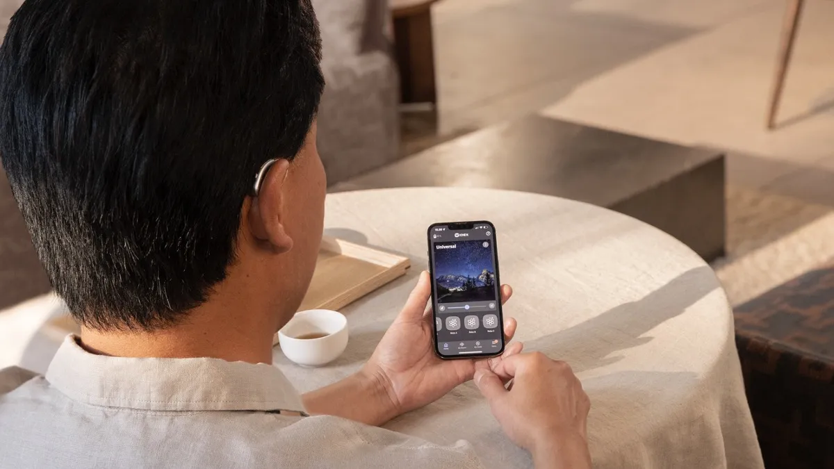 With most of the non-custom (over-the-ear) hearing aids offered at HearUSA, you can be fitted and walk out the door with the hearing aids on the same day. Here, a man adjusts his hearing aids in a cafe using the Widex MOMENT app.