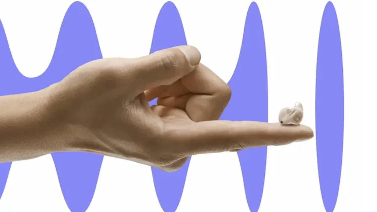 Hand with a small in-ear hearing aid resting on tip of the index finger