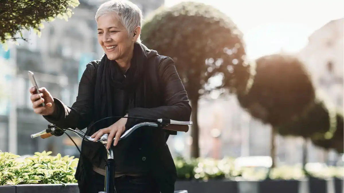 Photo of a women pausing on her bicycle to adjust her hearing aids
