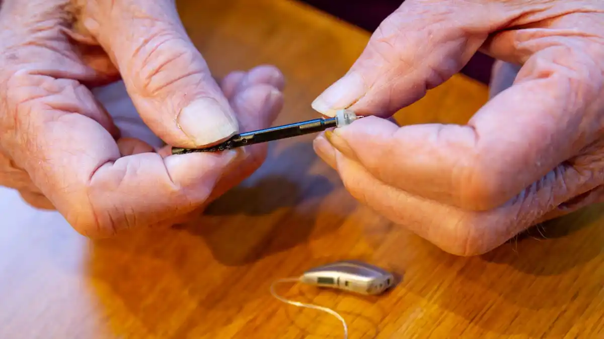 A senior holding a tool used for cleaning a receiver-in-canal (RIC) hearing aid.