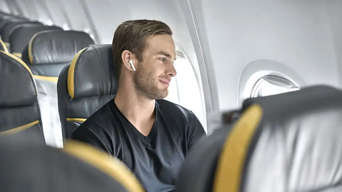 Man wearing earbuds sitting in the window seat on an airplane.