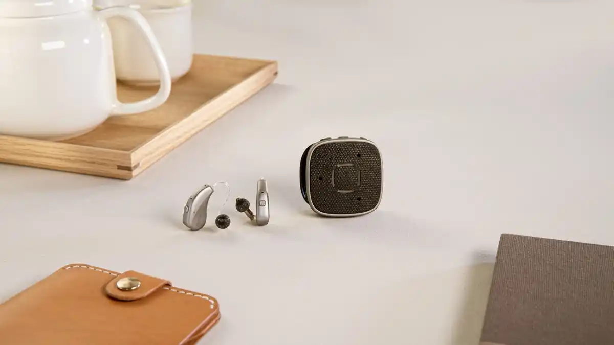 Widex MOMENT SHEER hearing aids pictured with the Widex Sound Assist, a five-in-one device designed to improve communication through partner and table microphone functionality, hands-free phone calls, direct streaming from any Bluetooth device, and remote control of these hearing aids.
