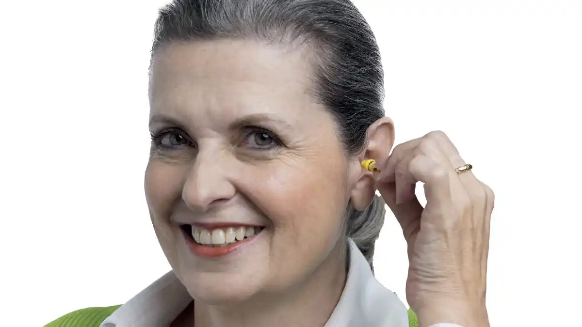 woman holding a tiny yellow Lyric hearing aid near ear