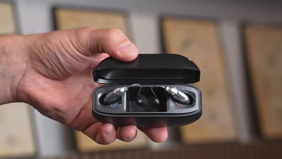 Silver Elehear Beyond Pro in their black open charging case, held by a hand in front of a blurred out background.