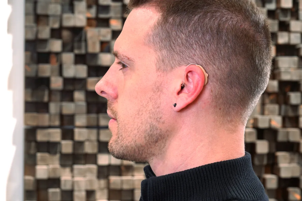 Beige hearing aid nestled behind ear of author with small wired leading to receiver in his ear canal