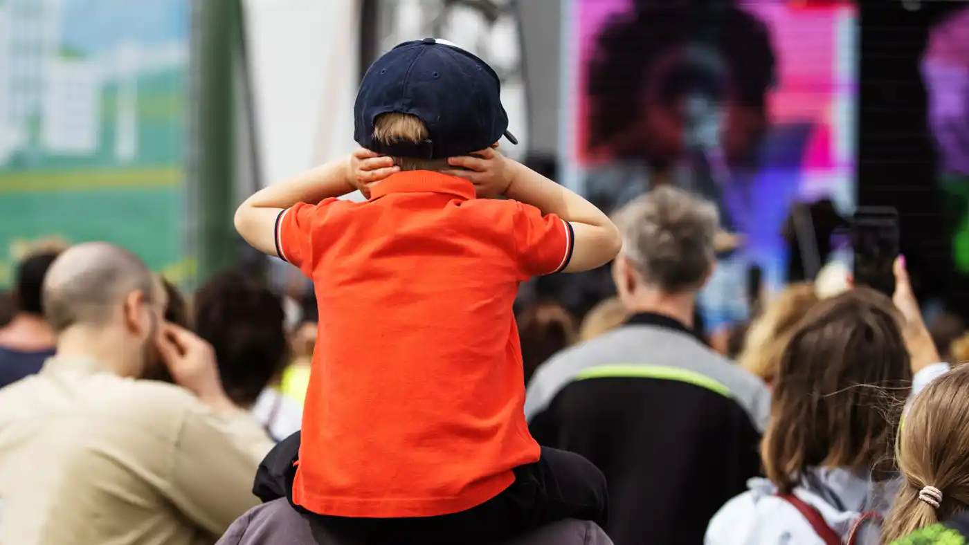 A young boy covers his ears at a loud concert.