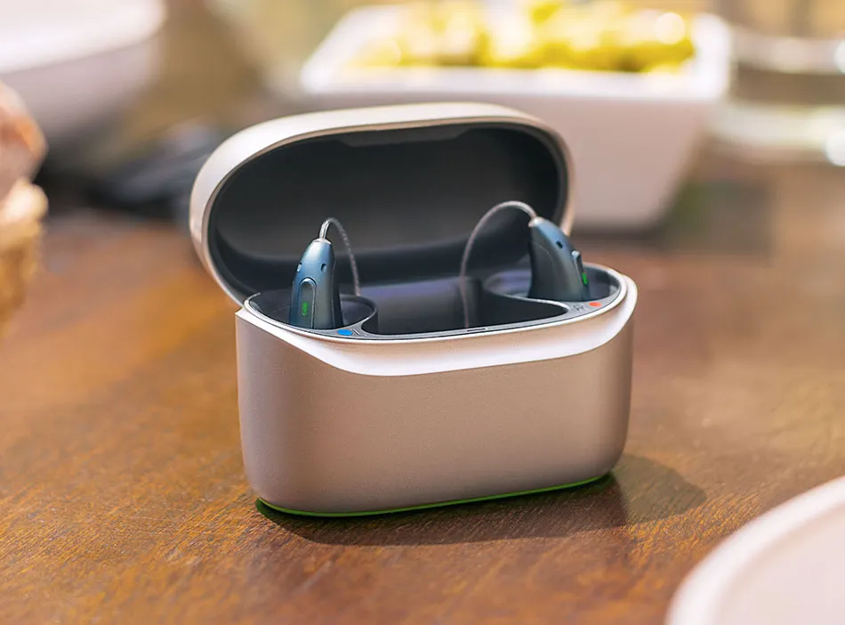 Gray Infinio hearing aids, one inside a tan charger and one outside