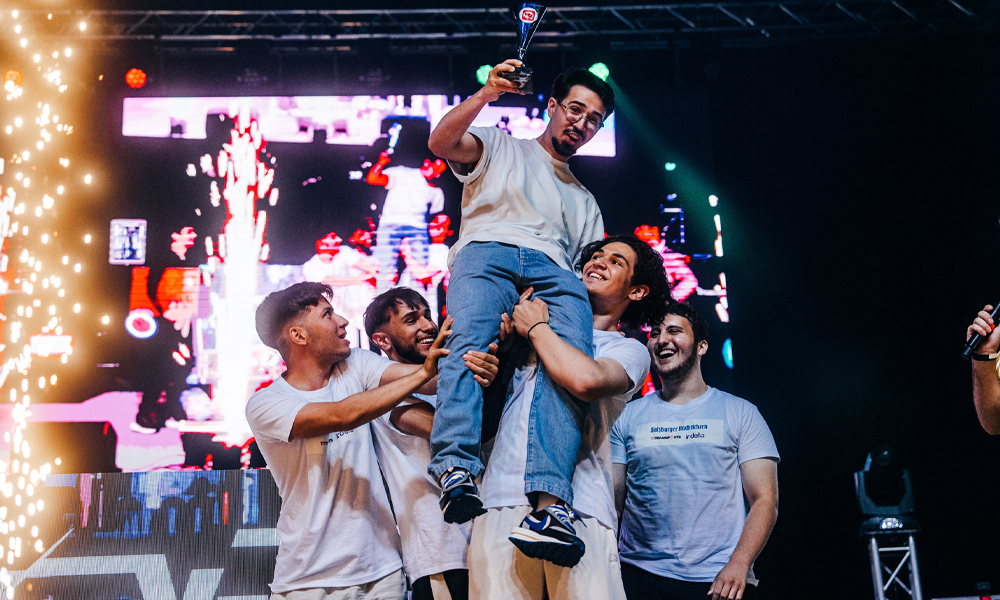 Gamer:innen lachen vor Freude in die Kamera mit einem Pokal in der Hand.