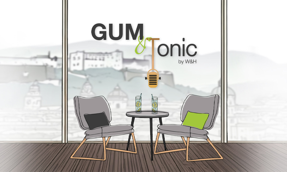 Podcast-Cover von "Gum & Tonic" mit zwei einander zugewandten Stühlen vor einem großen Fenster, das auf eine ruhige Stadtkulisse blickt. 